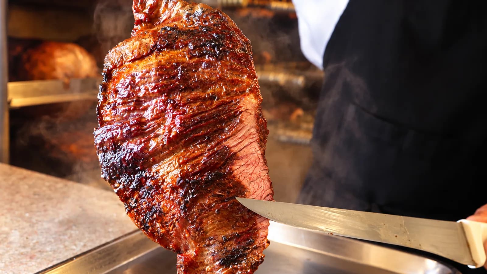 Carne na brasa sendo fatiada no espeto, no Fogão de Ouro