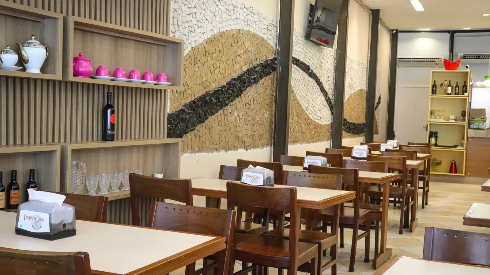 Painel de mosaico, prateleiras de louça e mesas postas no salão do Fogão de Ouro